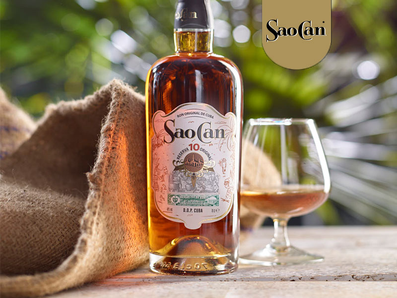 sao-can-reserva-original-10 Origini e caratteristiche del marchio Sao Can
Il marchio Sao Can, noto e diffuso a Cuba sin dalla metà del XIX secolo, ha le sue radici nelle piantagioni di canna da zucchero di Cárdenas, nell'ovest del paese. Queste piantagioni sono state coltivate storicamente dalla popolazione indigena Aruaco Taino. Il nome del marchio deriva dalla fusione tra SAOco e CANchánchara, due celebri cocktail cubani del tardo Settecento (molto prima della nascita del Mojito!). SAOCO è una bevanda semplice, ma dal gusto intenso e profondo, che si prepara con acqua di cocco, rum e ghiaccio. Viene preferibilmente servita in un guscio di cocco. CANCHÁNCHARA era invece una bevanda preparata dai "mambises" (soldati guerriglieri per l'indipendenza cubana), che mescolavano aguardiente con miele e succo di limone. Questa bevanda aveva lo scopo di aiutare i soldati a resistere al freddo e a proteggersi da malattie e problematiche respiratorie. Sao Can 10 Reserva Especial è un blend raffinato di diverse botti, con riserve molto invecchiate. Perfetto da gustare liscio, a temperatura ambiente, per apprezzarne l'intensità e la morbidezza, oltre al dolce e soave aroma con note di liquirizia e vaniglia.